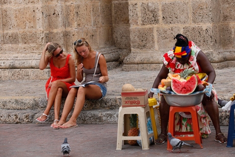 Khách du lịch ngồi xem bản đồ, trong khi, một phụ nữ bán hoa quả trên phố ở Cartagena, Colombia.