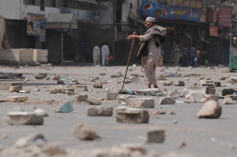 Một người ăn xin bị mù đang cố gắng đi qua đường phố đầy gạch vụn ở Karachi, Pakistan.