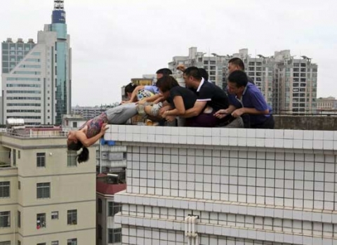 Nhóm người buộc phải nhoài người giữ lấy chân người phụ nữ để cô không bị ngã từ trên nóc của một khu nhà 9 tầng