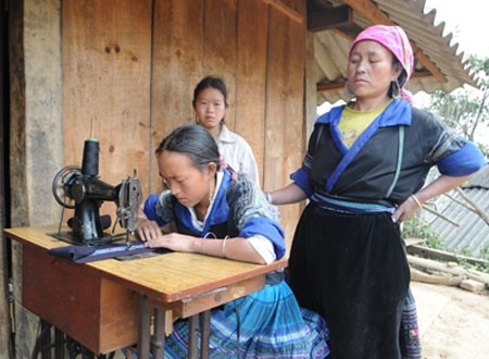 Em Hảng Thị Là (trái, con của nạn nhân Hảng A Chua và Thào Thị Của) cùng chị dâu ngày ngày vẫn cặm cụi may áo. Ảnh: Tuấn Nguyễn.